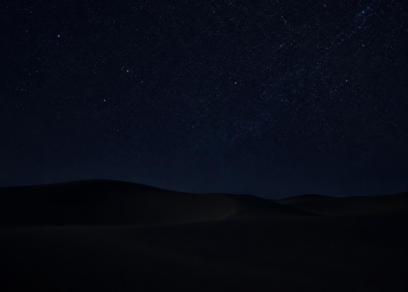 Céu nocturno densamente estrelado sobre um horizonte de dunas quase invisível